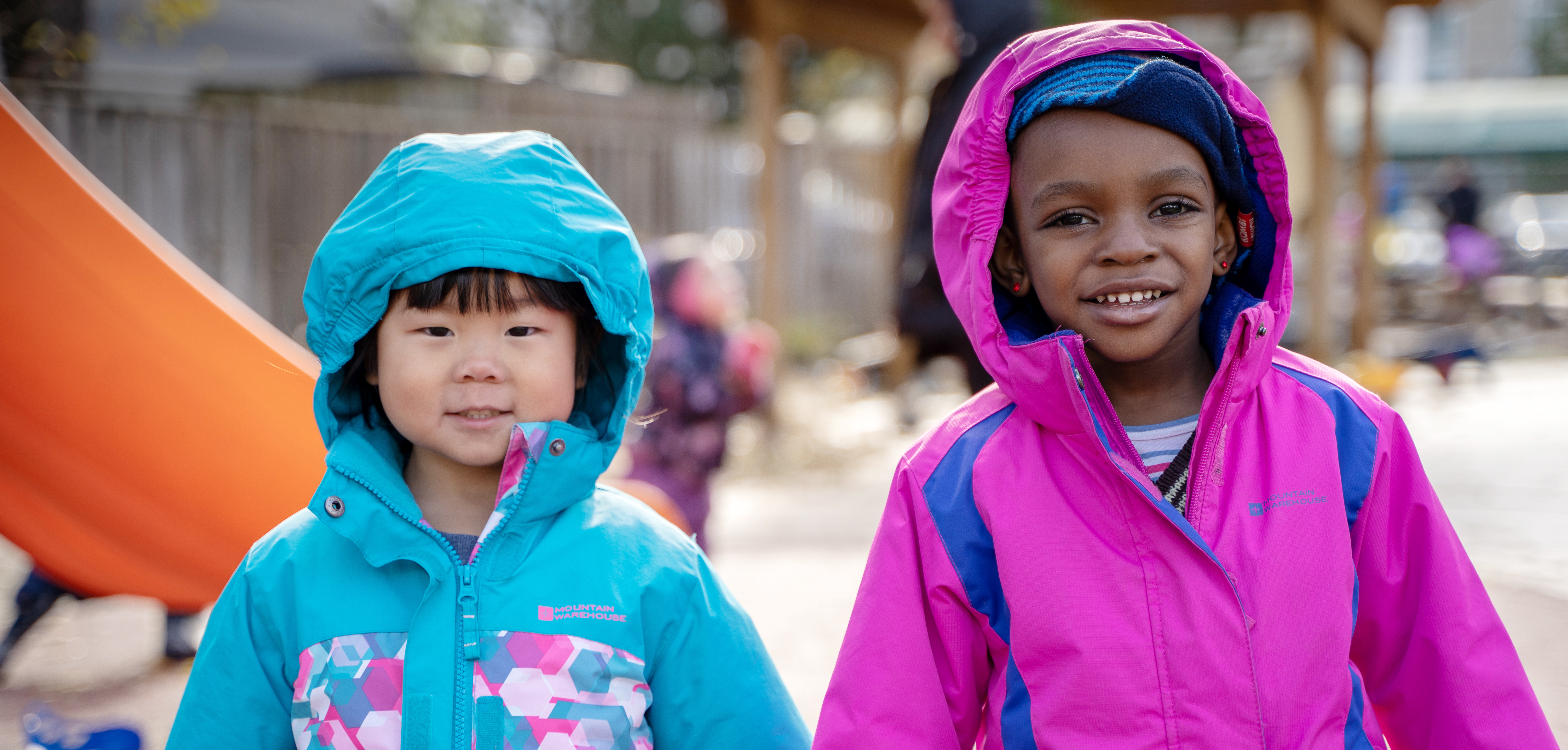 Two girls in bright spring coats, stay bundled while playing outside.