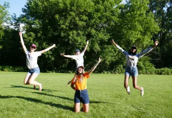 The YMCA Overnight Camp team jump and smile in a grassy field.