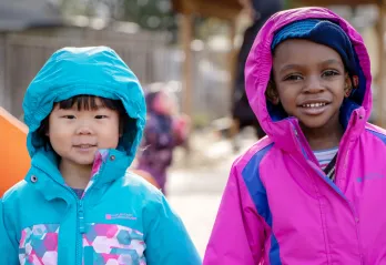 Two girls in bright spring coats, stay bundled while playing outside.