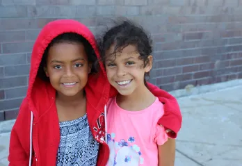 A girl in a red hoodie puts her arm around her friend in a pink t-shirt at YMCA Day Camp.