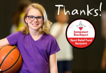 A young girl in a purple shirt smiles and holds a basketball.