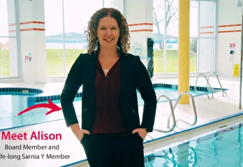Meet Alison: Board Member and Lifelong Sarnia Y Member. Alison, wearing a black suit and burgundy blouse, stands on the pool deck at the Sarnia YMCA.