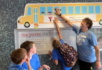 Three kids help a Y staff member update the Fill The Bus tracker at the Chatham YMCA.