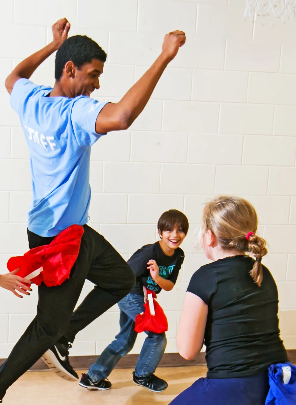 Kids chasing a staff member, playing a game of flags inside a gym.