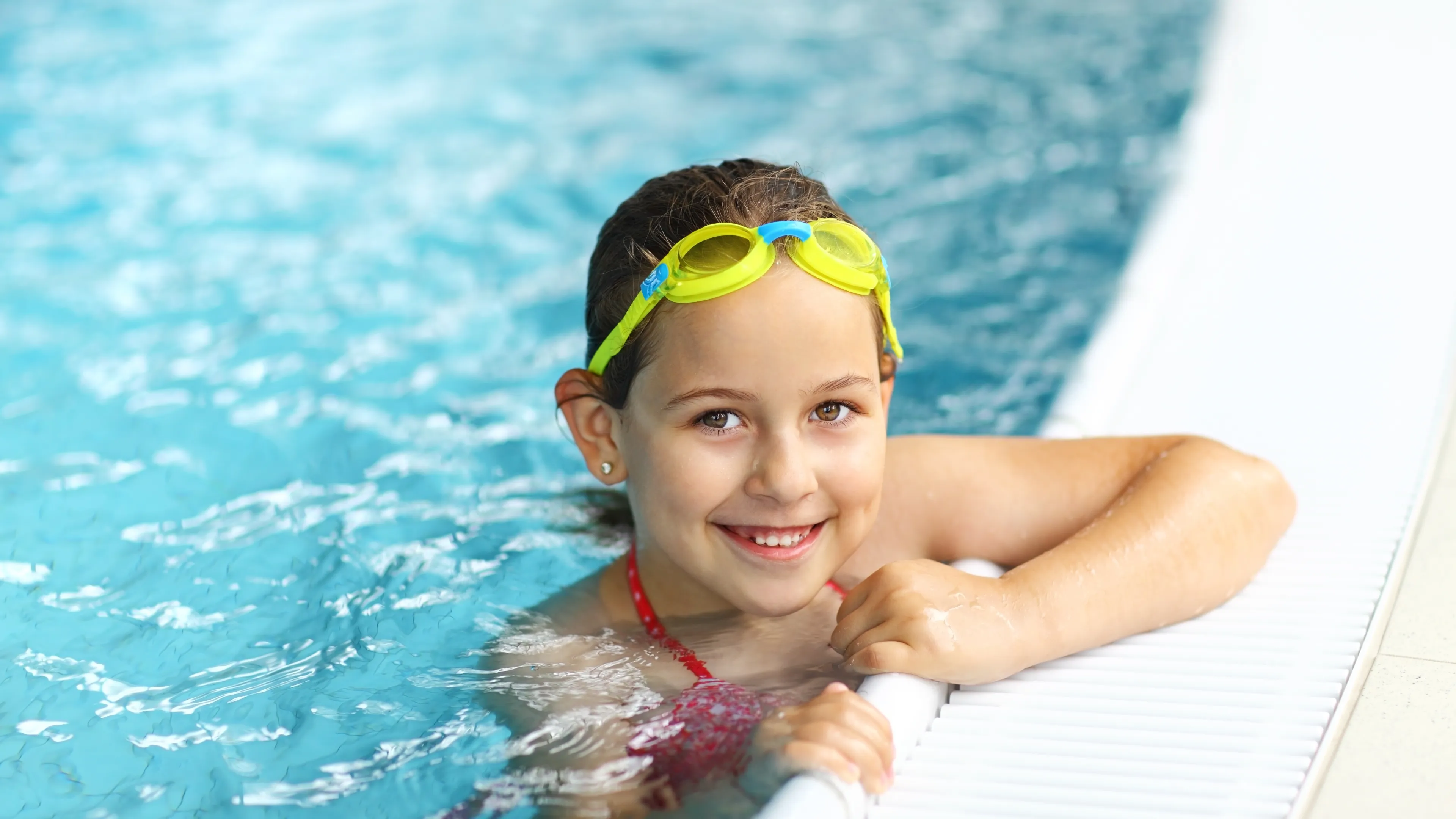 Girl holding onto the edge of the pool smiling.