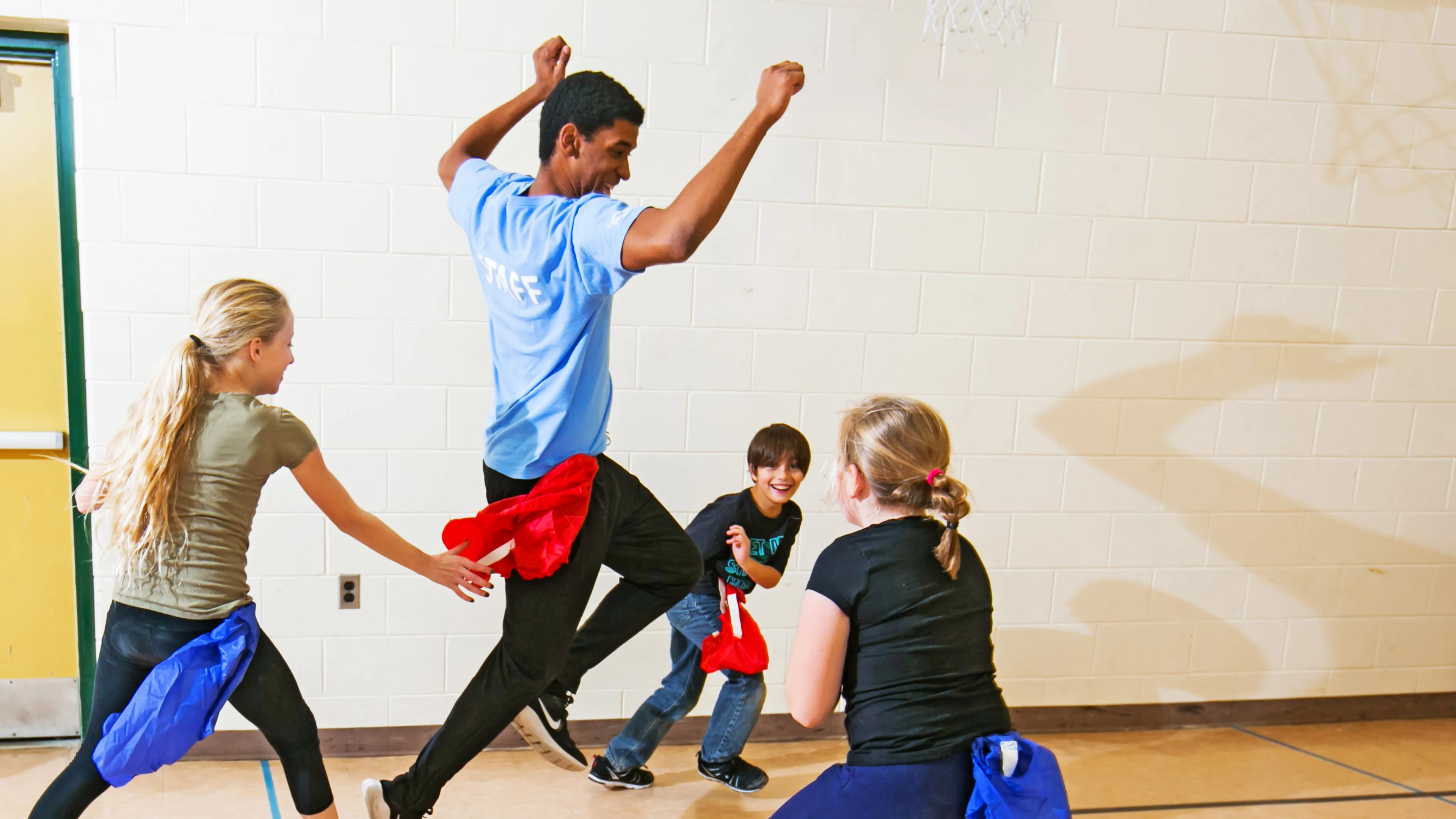 Kids chasing a staff member, playing a game of flags inside a gym.