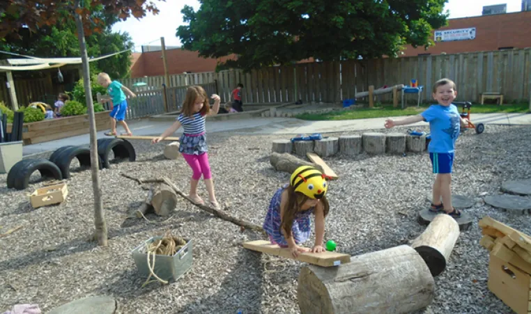 A group of four children explore a YMCA outdoor play space during the summer.