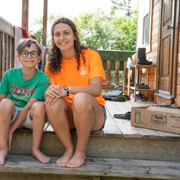 A counsellor and camper smile and sit together on a wooden deck.