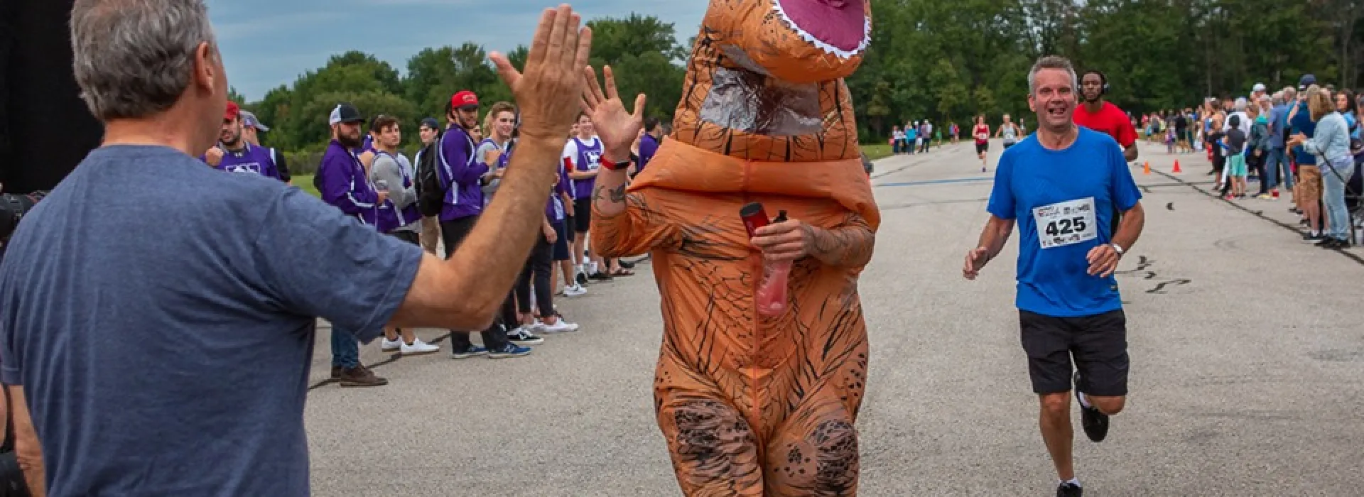 A participant in a T-Rex costume high fives as they cross the finish line.