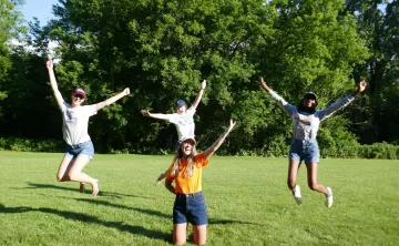 The YMCA Overnight Camp team jump and smile in a grassy field.