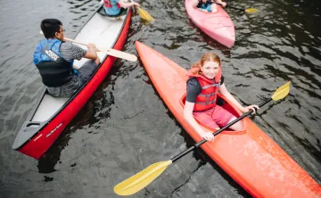 A group of kids paddle on the lake in canoes and kayaks.