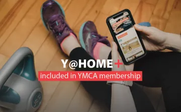 Y@HOME+ included in YMCA membership. Image: a woman in running shoes watches a workout on her mobile device next to a kettlebell.