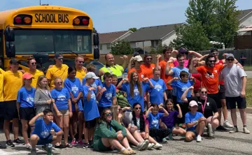 Participants of "Push The Bus" at the Jerry McCaw Family YMCA in Sarnia smile and pose in front of a school bus.
